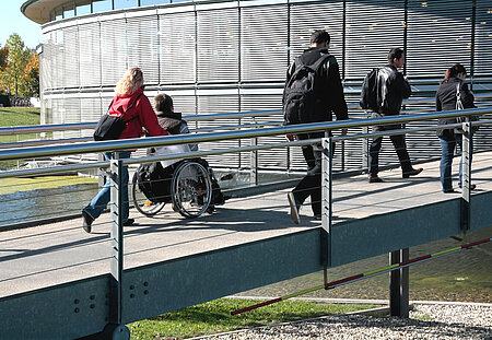 Das Bild zeigt fünf Personen auf einer Brücke, vier Personen zu Fuß und eine Person im Rollstuhl. Bildnachweis: Foto: OTH Regensburg